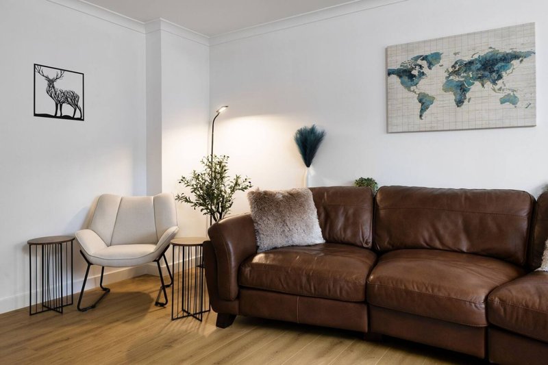 Modern living room with brown leather sofa, cream armchair, wooden side tables and wall art
