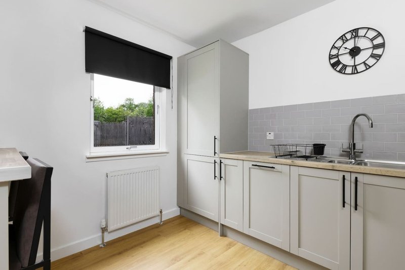 Modern kitchen with cream cabinets, gray tile backsplash, wooden floor and wall clock