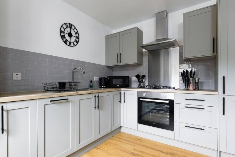 Modern kitchen with white cabinetry, grey tile splashback, wooden countertop and stainless steel appliances