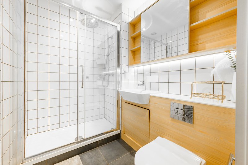 Modern bathroom with white tile walls, wooden vanity, glass shower enclosure and mirror.