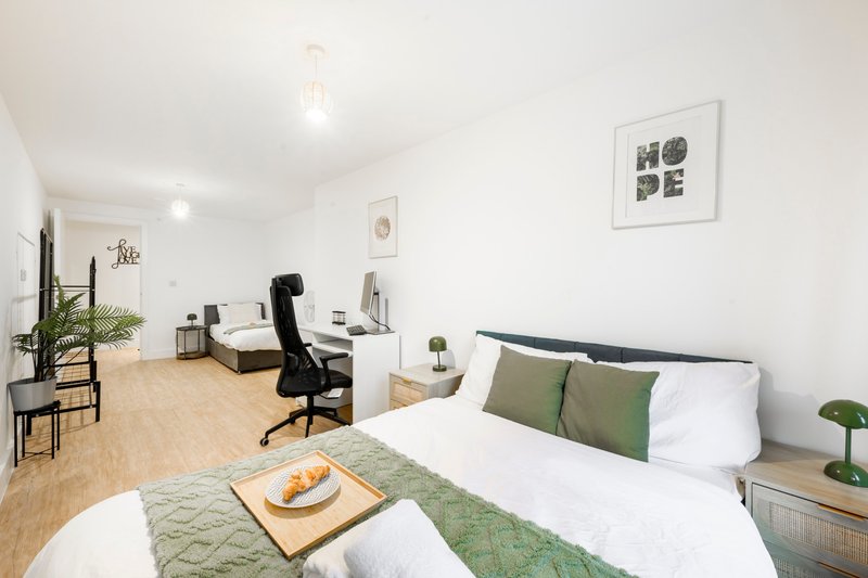 Bright studio bedroom with double bed, desk workspace, wooden flooring and wall art