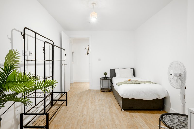 Bright bedroom with black metal bed frame, wooden flooring, potted plant, and white fan