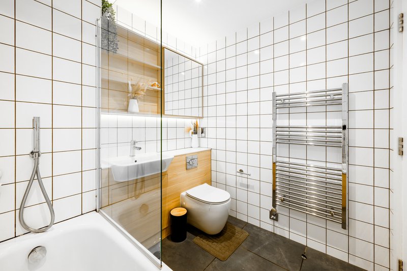 Modern bathroom with white tiles, wooden accents, toilet, basin, shower and heated towel rail