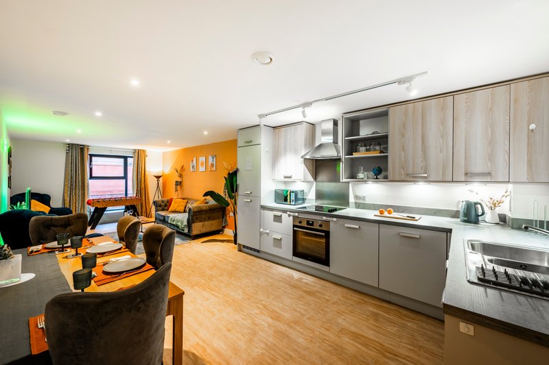 Open-plan living and kitchen area with orange accent wall, brown furniture, and modern appliances