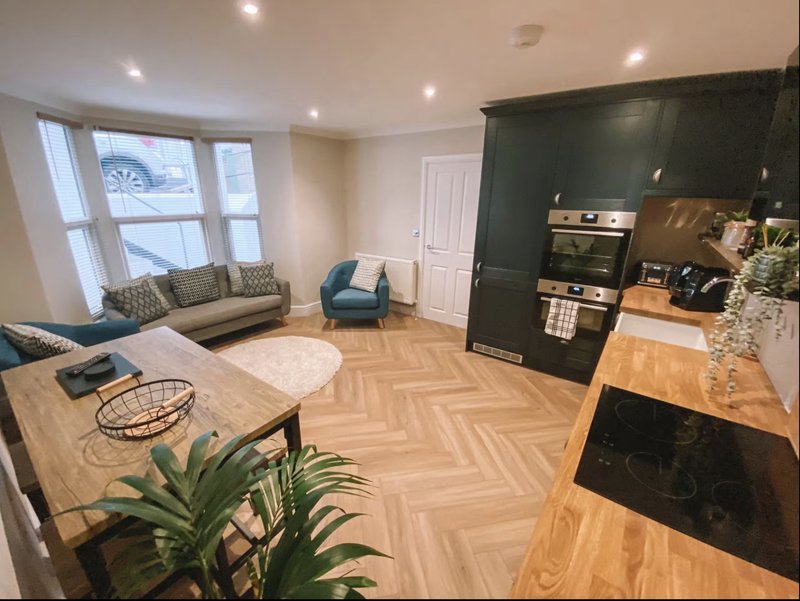 Open-plan living and kitchen area with herringbone flooring, seating area, and fitted kitchen