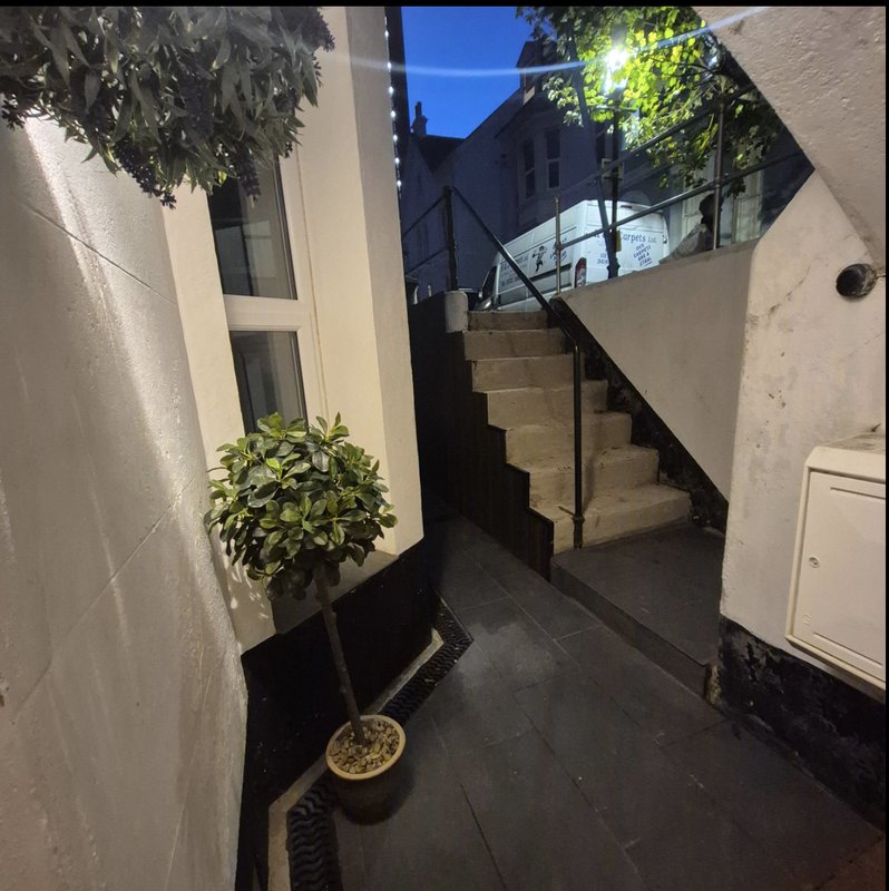 Narrow outdoor courtyard with potted plant, stairs, and modern glass railing