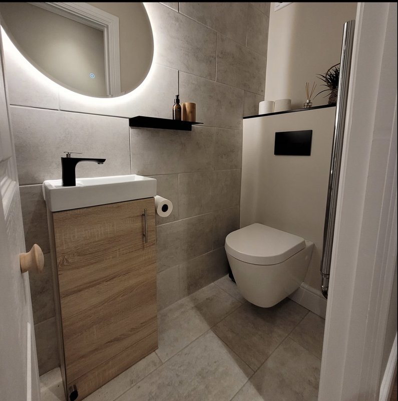 Modern bathroom with wall-mounted sink, toilet, illuminated mirror and tiled walls