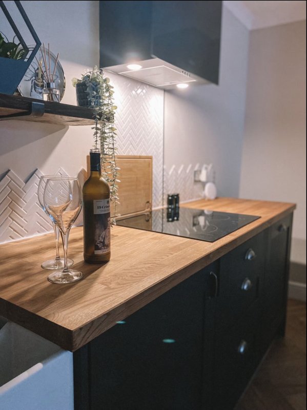Modern kitchen with wooden countertop, black cabinetry, wine bottle and glass on counter