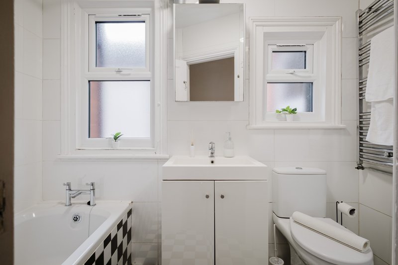 Modern bathroom with white suite, sink vanity, bathtub, toilet, and frosted windows
