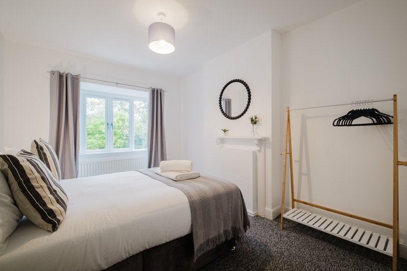 Bright bedroom with double bed, wooden clothes rail, round mirror and large window
