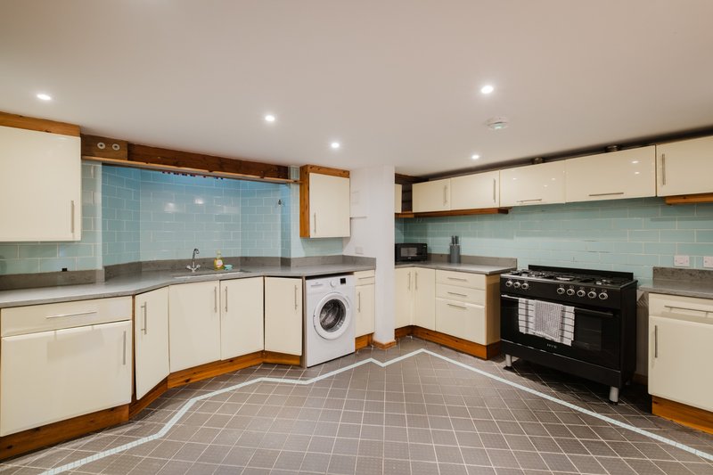 Modern kitchen with cream cabinets, black range cooker, washing machine, and tiled flooring
