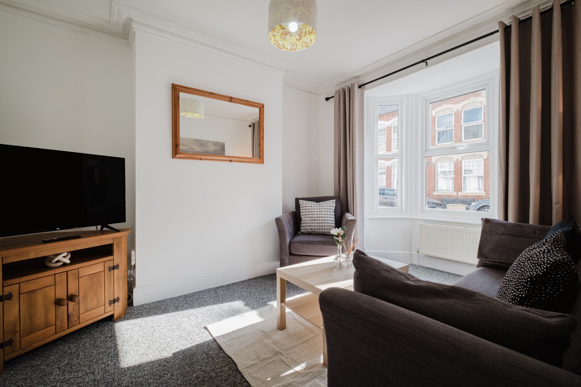 Bright living room with dark sofas, wooden TV stand, framed mirror and large windows