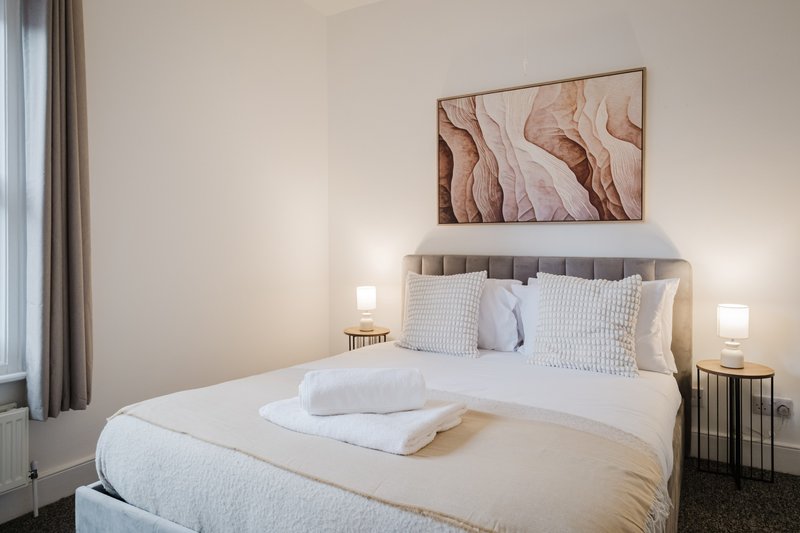 Modern bedroom with double bed, white bedding, framed abstract artwork, and bedside lamps