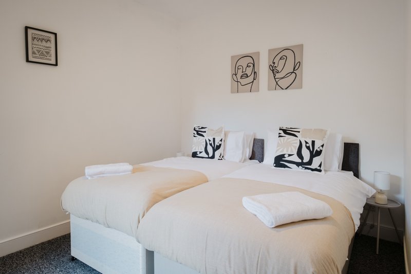 Modern bedroom with two white beds, black and white decorative pillows, minimalist line-art wall prints