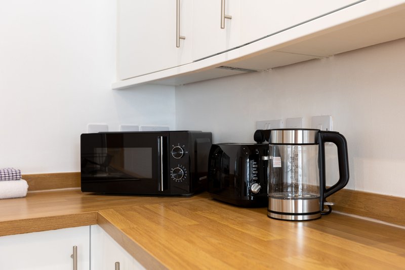 Kitchen countertop with microwave, coffee maker and kettle under white cabinets