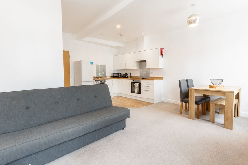 Open-plan living space with grey sofa, dining table, and kitchen area with wooden cabinetry