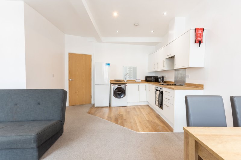 Open-plan kitchen and living area with white cabinetry, wooden countertop, washing machine, and grey sofa