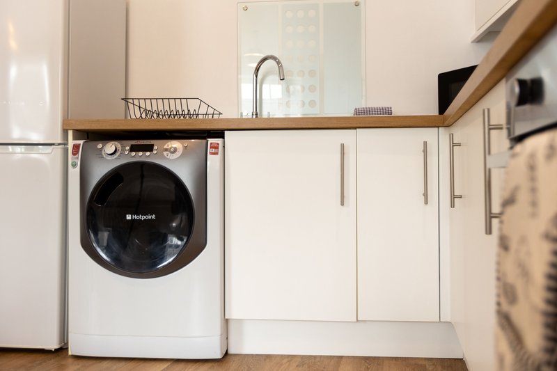 Modern kitchen with washing machine, white cabinetry, wooden countertop and sink