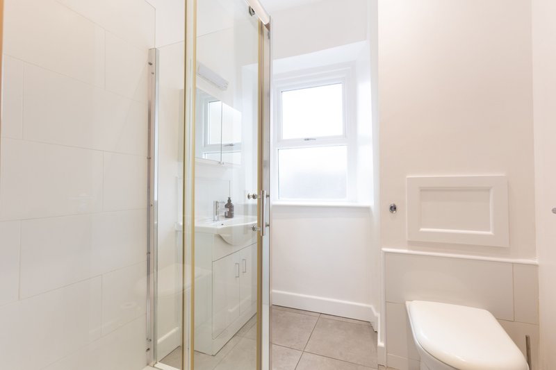 Bathroom with shower enclosure, toilet, sink, and window with natural light