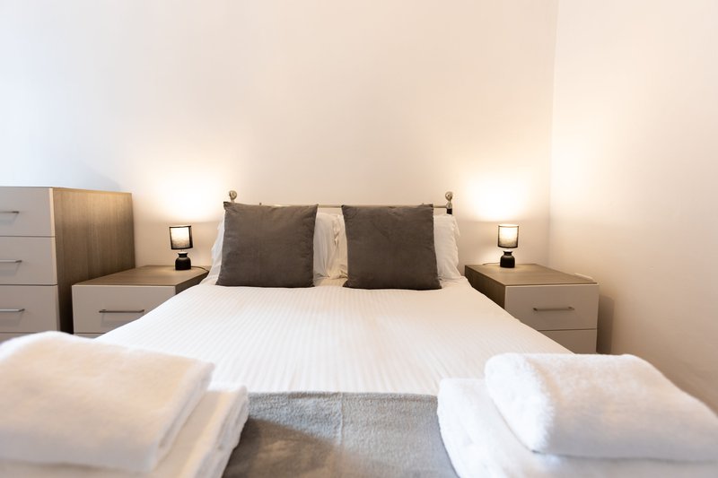 Modern bedroom with double bed, dark headboard, bedside tables with lamps and white pillows