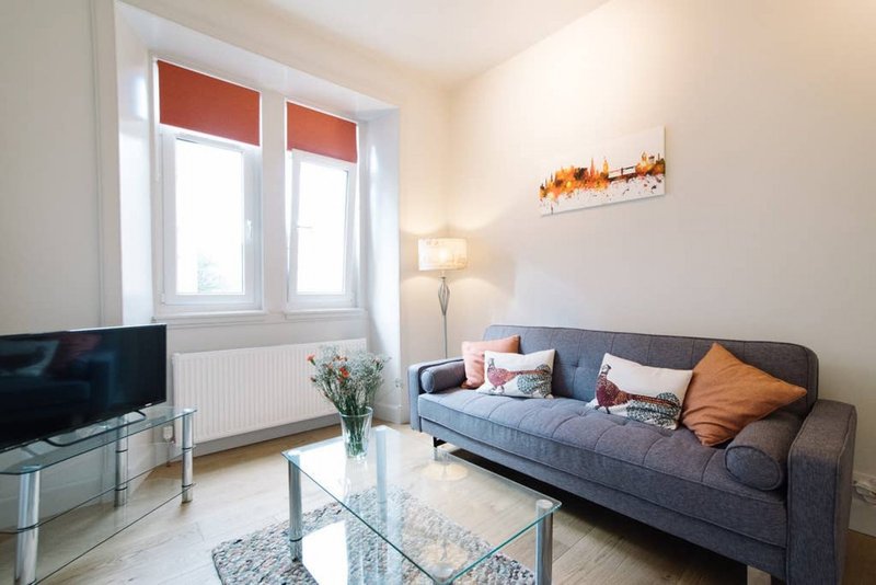 Bright living room with gray sofa, TV, glass coffee table and red window blinds