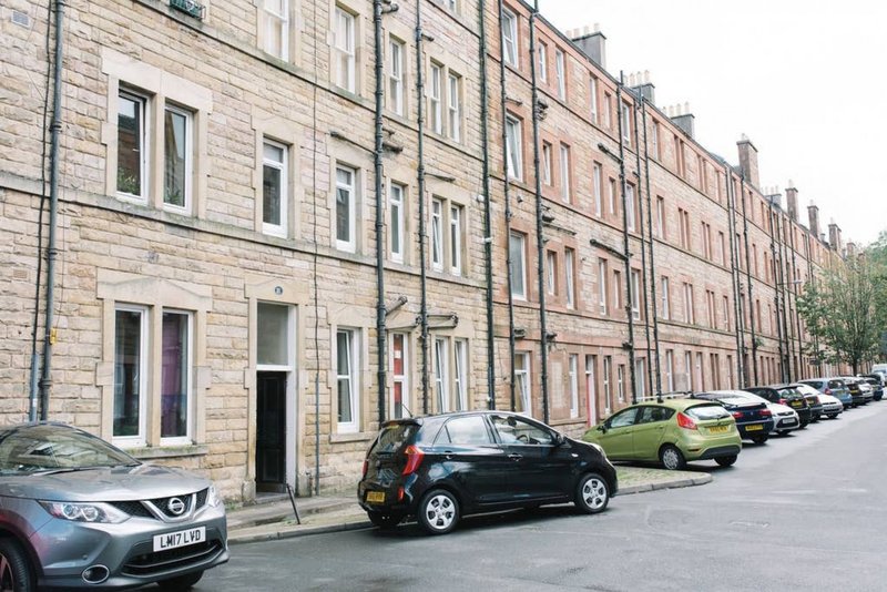 Row of traditional stone tenement buildings with parked cars on street