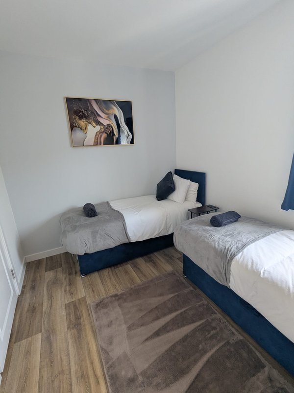Twin bedroom with two single beds, navy headboards, white bedding, wooden floor and wall art