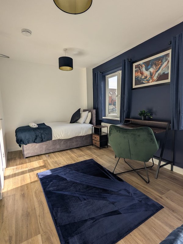 Modern bedroom with single bed, dark blue feature wall, desk chair and wooden flooring