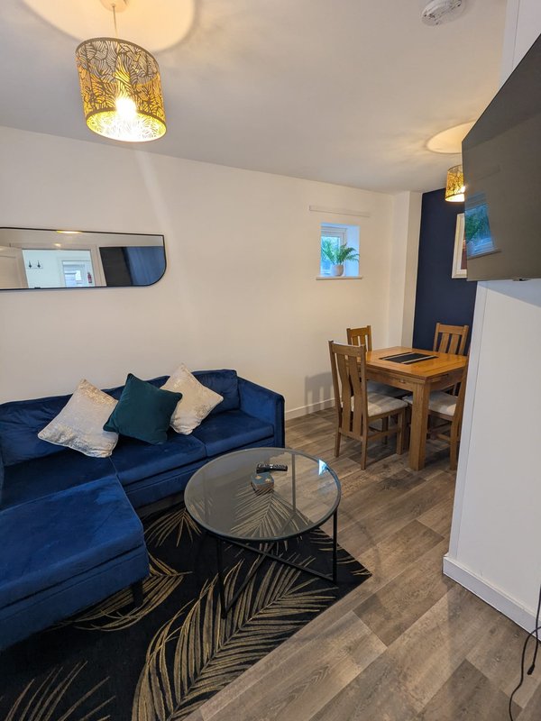 Open-plan living area with blue sofa, dining table, wooden chairs and pendant lighting