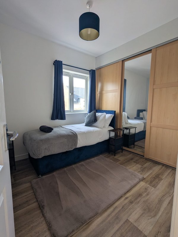Modern bedroom with double bed, wooden flooring, mirrored wardrobe and window with blue curtains