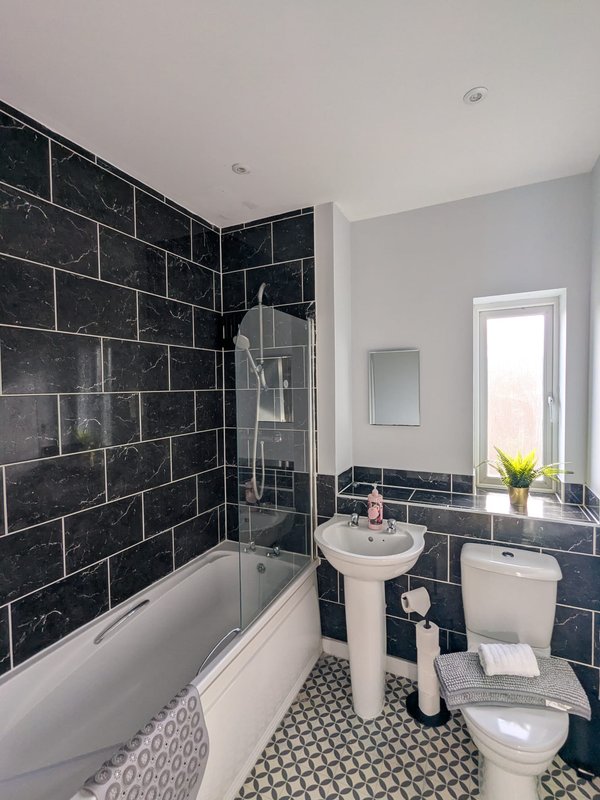 Modern bathroom with black marble tiles, white bathtub, pedestal sink and toilet
