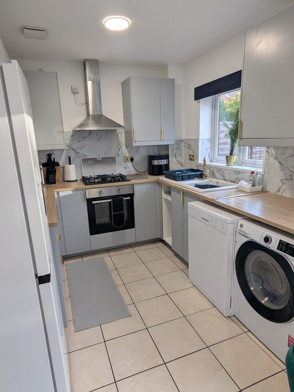 Modern kitchen with white cabinetry, black gas range, washing machine, and marble splashback