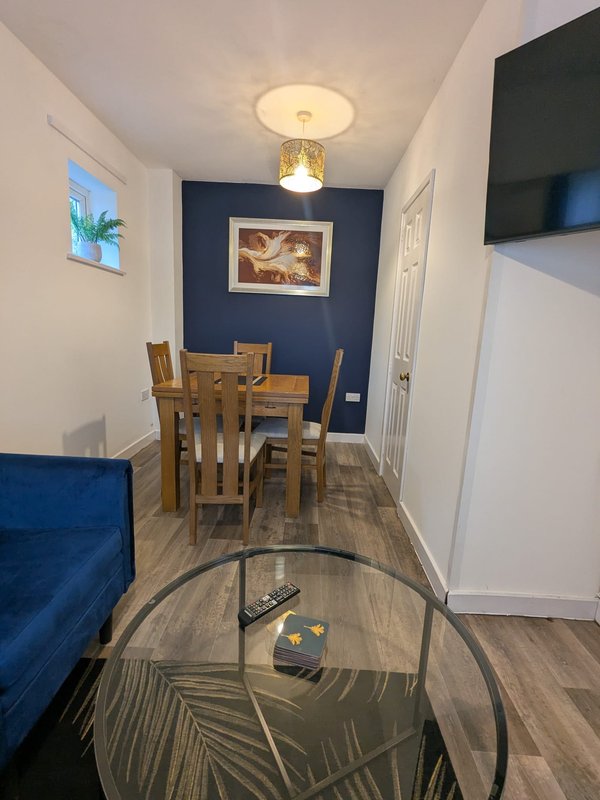 Dining area with wooden table and chairs, blue accent wall, sofa, and mounted TV