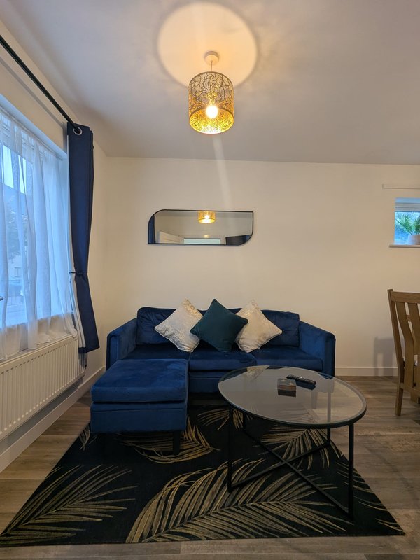 Living room with blue corner sofa, black patterned rug, round coffee table and ceiling light