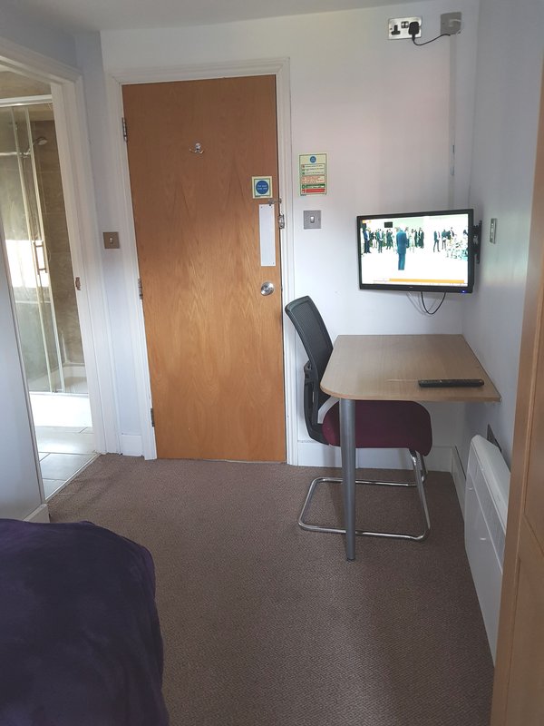 Small bedroom with desk, chair, monitor, and brown wooden door
