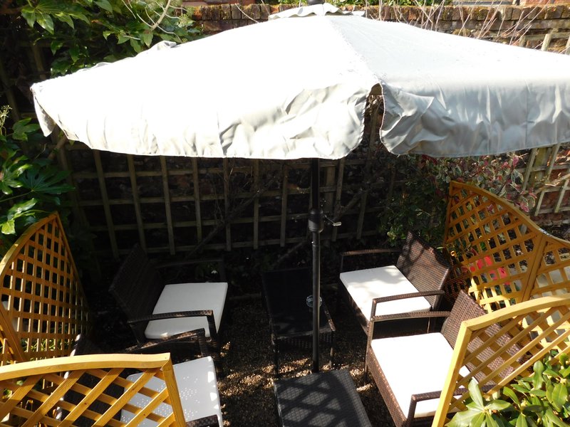 Shaded garden seating area with white umbrella, yellow lattice panels and cushioned chairs