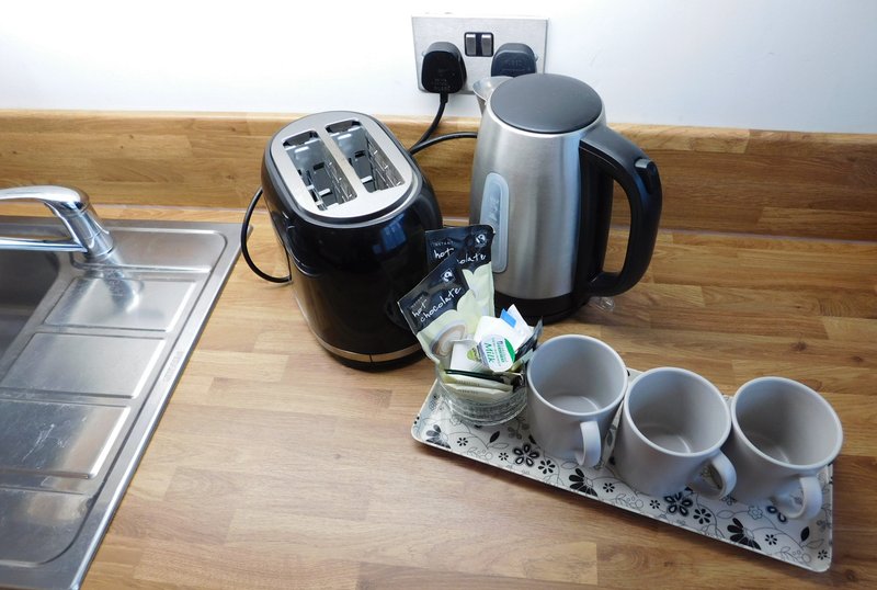 Kitchen counter with toaster, kettle, coffee maker, mugs and wall outlet