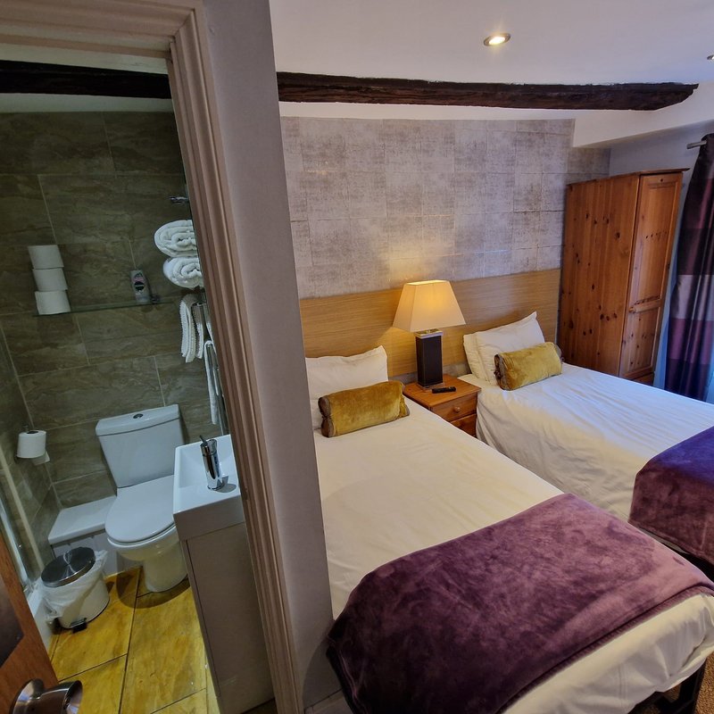 Bedroom with twin beds, wooden headboard, en-suite bathroom visible through open door