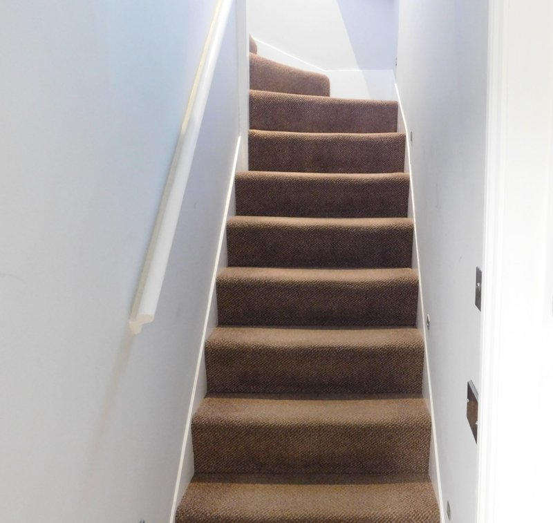 Carpeted staircase with brown treads, white walls and handrail, leading upward