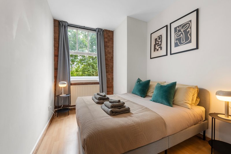 Modern bedroom with double bed, green cushions, framed wall art, and large window with brick detailing