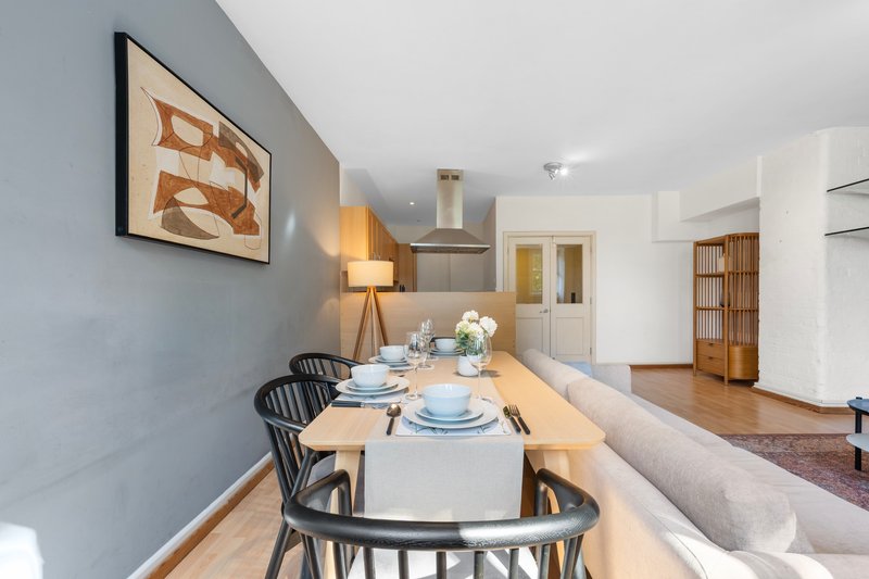 Dining area with wooden table, black chairs, and place settings, adjacent to kitchen