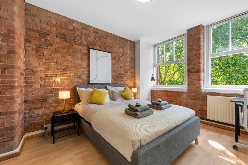 Bright bedroom with exposed brick walls, double bed, wooden floor and large windows