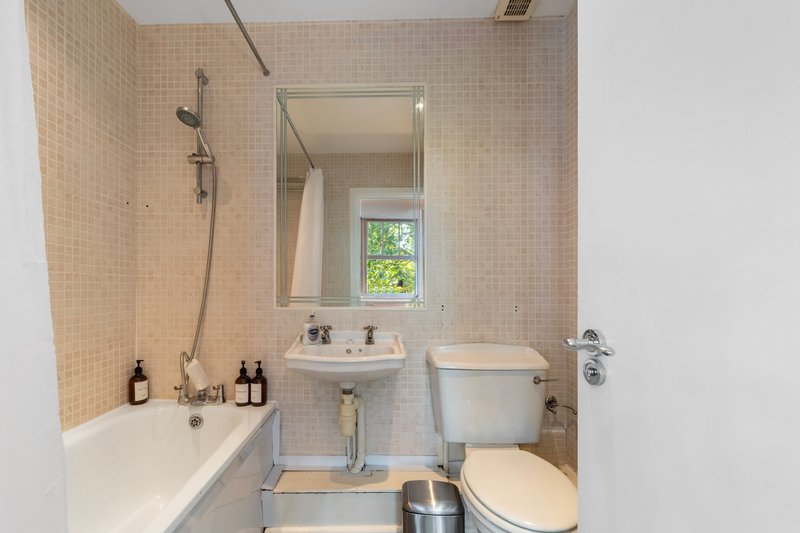 Compact bathroom with bathtub, pedestal sink, toilet, small window and beige tile walls