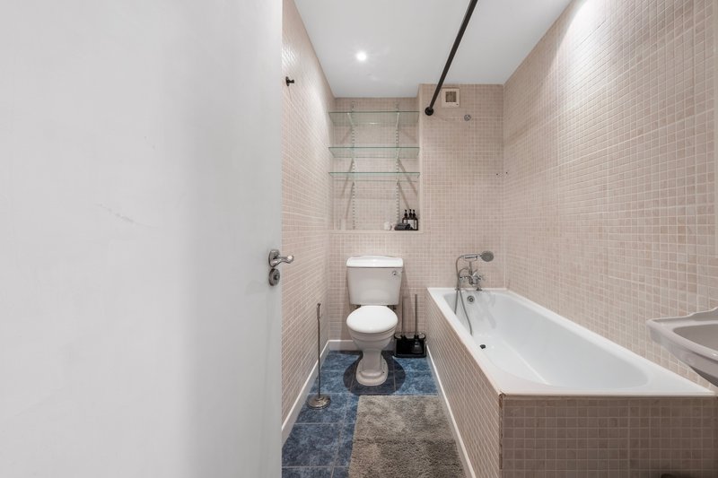 Modern bathroom with toilet, bathtub, sink, tiled walls and recessed lighting