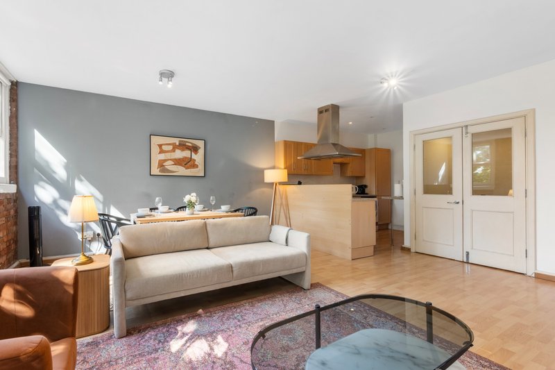 Open-plan living area with beige sofa, wooden kitchen, grey accent wall and wooden flooring