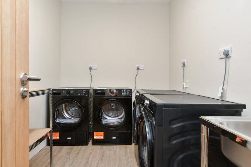 Laundry room with black front-load washer and dryer, utility sink, and white walls