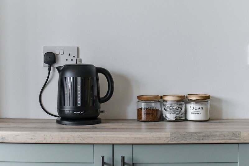 Kitchen counter with black electric kettle, power outlet, and three labeled storage jars