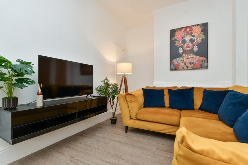 Living room with mustard yellow sofa, blue cushions, wall-mounted TV, and colorful artwork