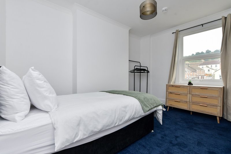 Bright modern bedroom with double bed, white bedding, wooden dresser and blue carpet