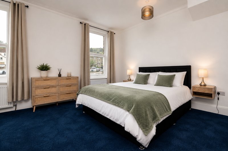 Bright modern bedroom with double bed, wooden dresser, navy carpet and large windows